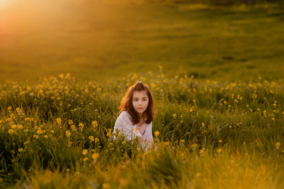 Young girl sitting in the field of yellow mustard flowers playing with a flower.