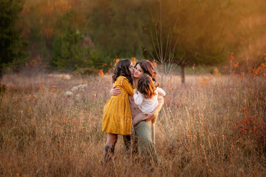 Mother with her two daughters in the hills of east bay in California smiling at the camera while children are hugging and kissing her.