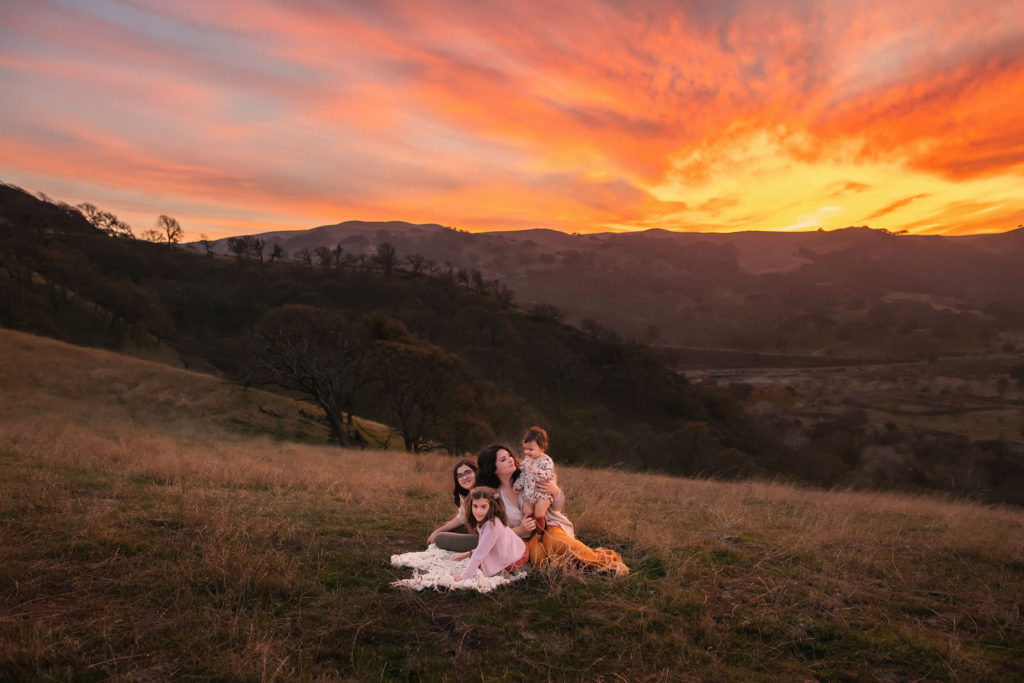 Mother with her three daughters in the hills of east bay in California posing for photos against beautiful golden sunset.