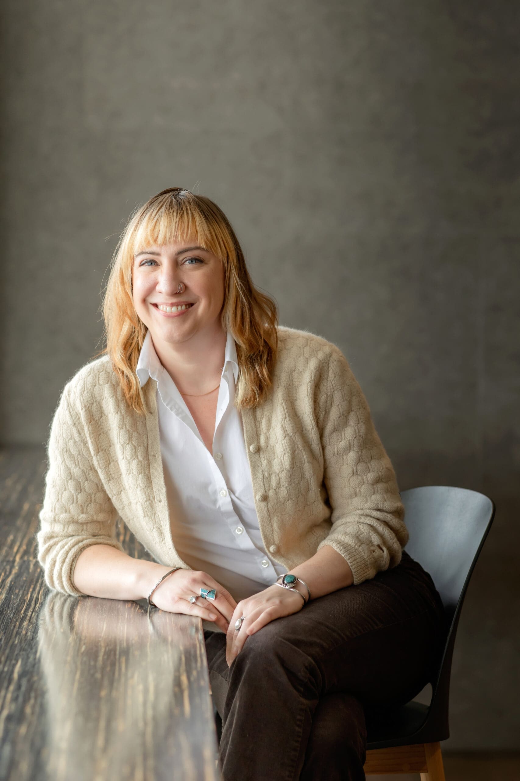 A blond woman sitting at the window smiling at the camera for her headshot photoshoot