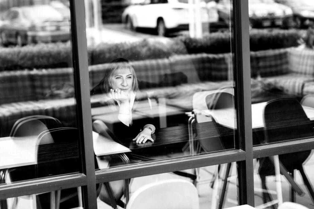 Business woman looking through a window while being photographed for her website.