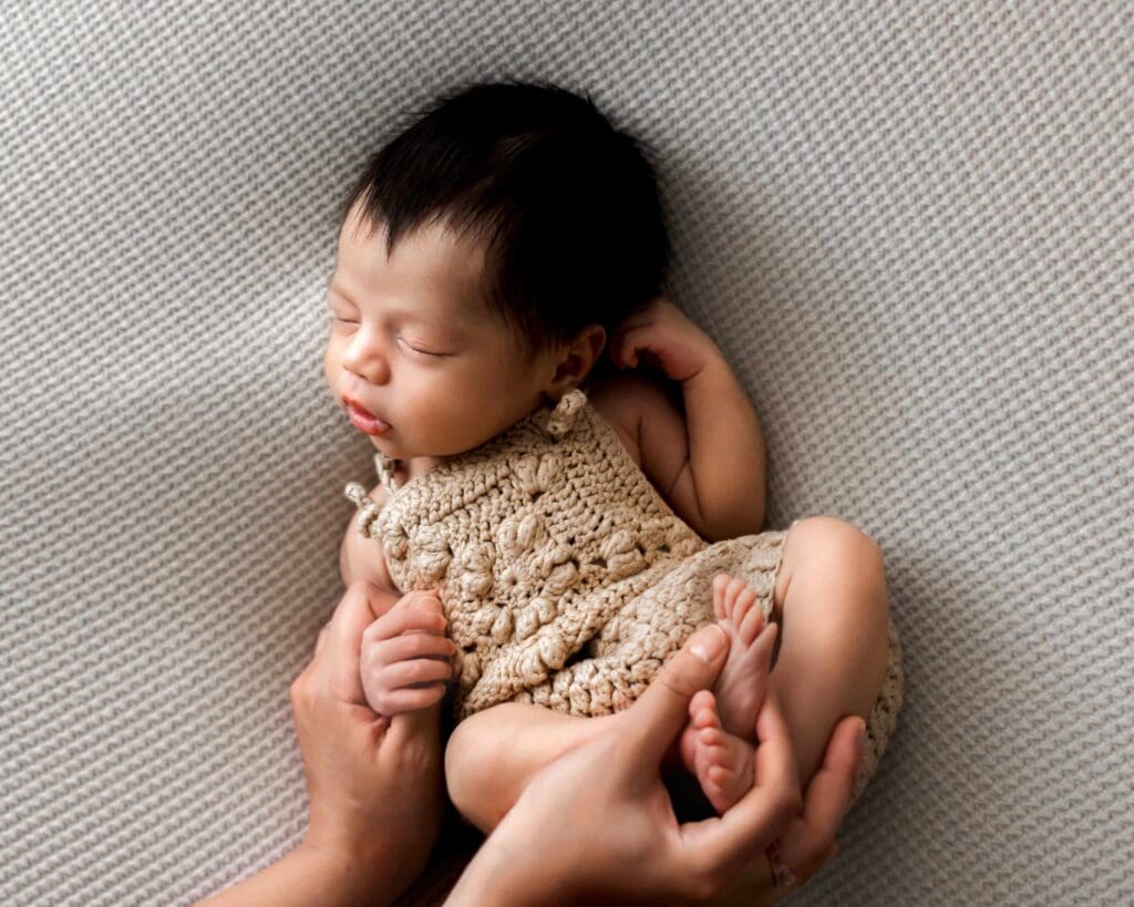 Newborn fingers holding mother’s hand wearing one-of-a-kind outfit