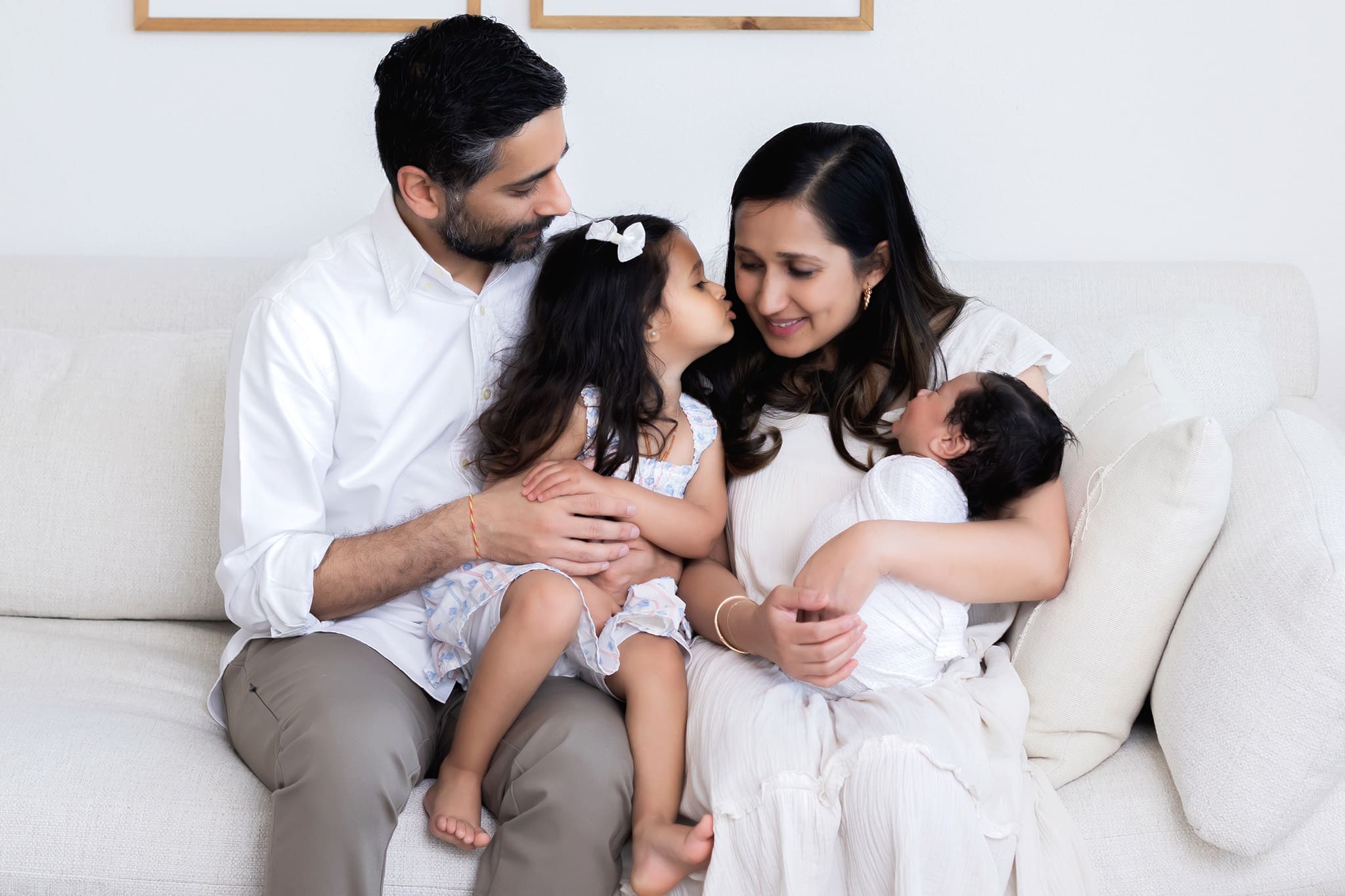 Family of four with a newborn baby and toddler girl kissing her mom